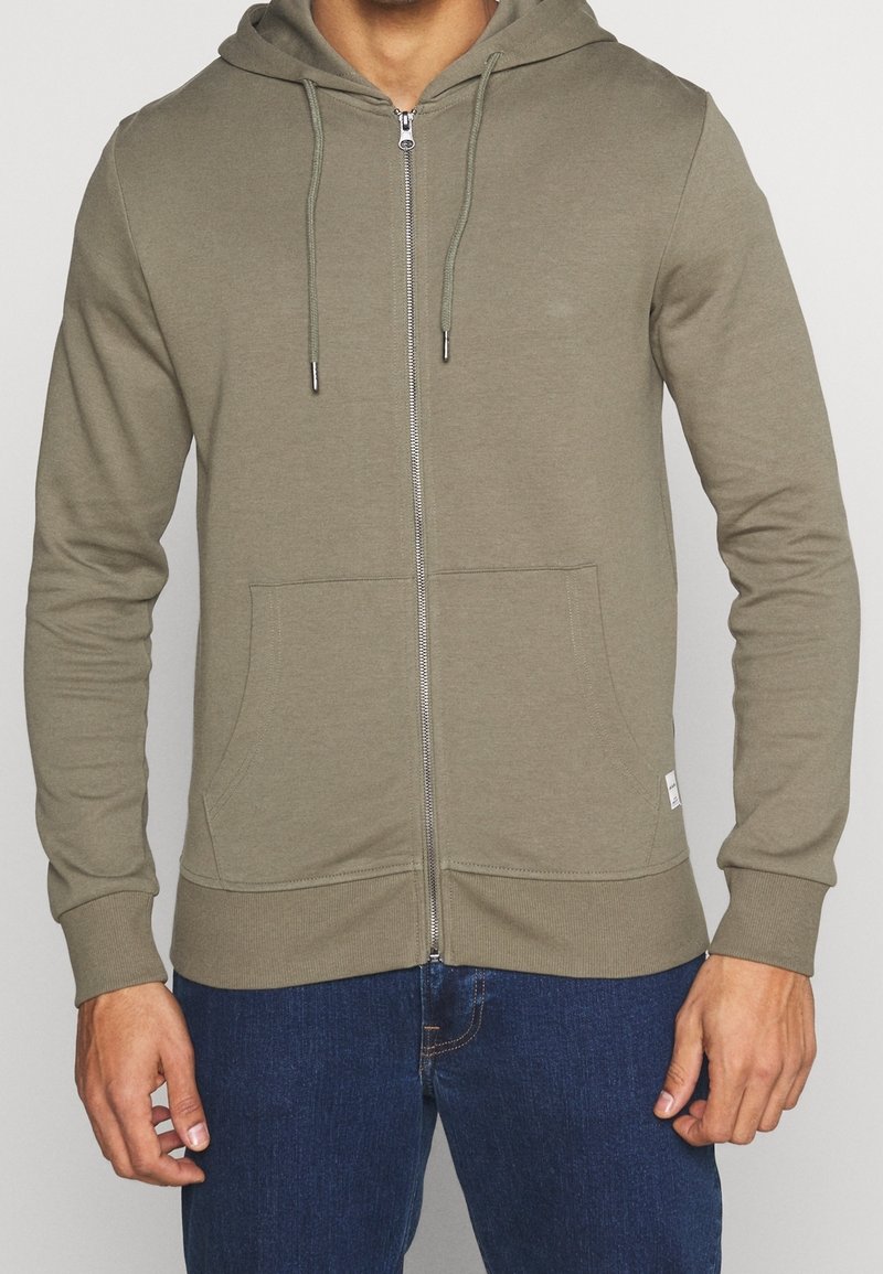 Sudadera con capucha color verde oliva con cremallera, confeccionada en material suave, con cremallera frontal, cordones ajustables y bolsillos laterales. Detalles de puños y bajo acanalados.