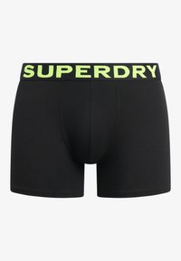 Boxers noirs avec une texture unie, arborant un logo "SUPERDRY" vert fluo sur la ceinture élastique. Conçus pour le confort et l'ajustement.