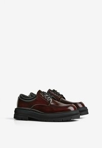 Scarpe in pelle marrone lucida con suole in gomma nera, punta rotonda e sei fori per i lacci. Presentano cuciture a contrasto e un tacco arrotondato.