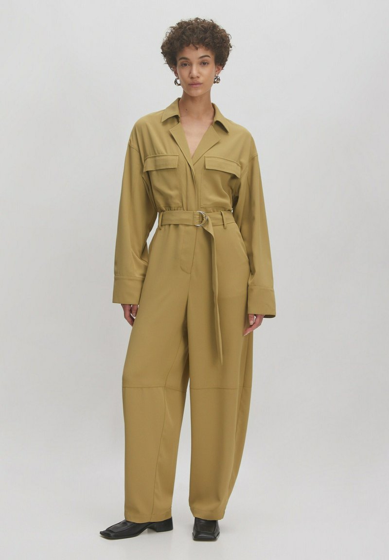 Helles olivgrünes Jumpsuit mit tailliertem Gürtel, großen Brusttaschen und weitem Bein. Hergestellt aus glattem, leicht glänzendem Stoff.