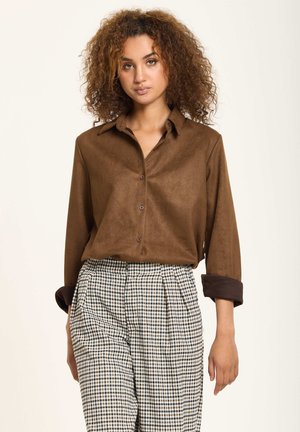 Brown button-up shirt with a textured finish, featuring a collar and rolled sleeves, paired with high-waisted plaid trousers.