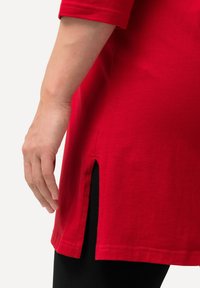 Rote Baumwolltunika mit kurzen Ärmeln und seitlichen Schlitzen, aus weichem Material mit geradem Saum, kombiniert mit schwarzen Leggings.
