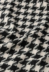 Tessuto tessuto con un motivo a scacchi bianco e nero. La texture appare morbida con filati intrecciati visibili e blocchi di colore alternati.