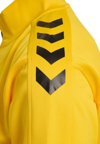 Tissu jaune vif avec quatre bandes chevrons noires pointant vers le bas, alignées verticalement sur une manche.