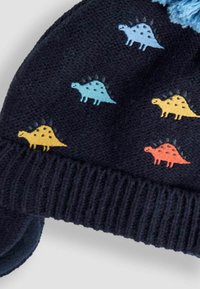 Pletená tmavomodrá čiapka s rebrovaným okrajom, zdobená viacfarebnými vzormi dinosaurov v oranžovej, žltej, modrej a tyrkysovej farbe. Mäkká štruktúra.