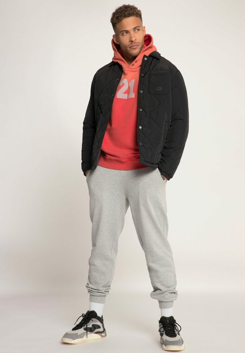 Giacca nera trapuntata, felpa rossa con stampa "21", pantaloni grigi, e sneaker grigi. Texture morbide, colori a contrasto, design casual.
