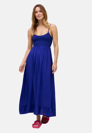 Largo vestido maxi azul con un cuerpo ajustado y cintura fruncida, con tirantes finos y un dobladillo con volantes. Llevado con sandalias de color rosa brillante.
