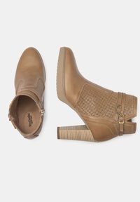 Bottines marron avec une tige en cuir texturé, un panneau latéral perforé, des doubles boucles et un talon épais à rayures. La semelle présente des détails de grip.