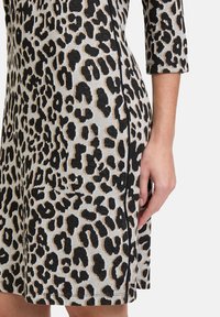 Leopardenmuster Kleid in Grau, mit kurzen Ärmeln und lockerer Passform. Der Stoff hat eine strukturierte Optik mit schwarzen und beige Mustern.