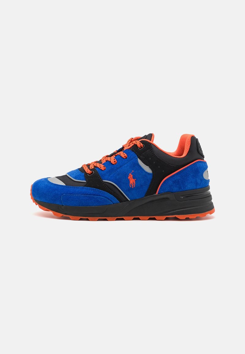 Chaussure de sport en suède bleue avec des accents noirs, des lacets orange et des détails. Équipée d'une semelle texturée et d'éléments réfléchissants.