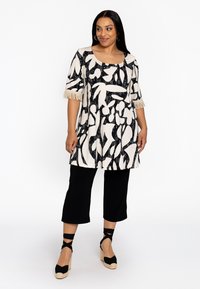 Zwart-wit gestreepte tuniek met franjes mouwen, gecombineerd met zwarte cropped broeken en zwarte espadrille wedges. Gladde stoftextuur.