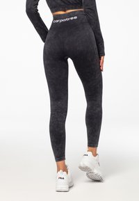 Černé, strukturované legíny s vysokým pasem, na kterých je logo "carpatee". V kombinaci s bílými sportovními botami, které ukazují elegantní, těsně přiléhající design.