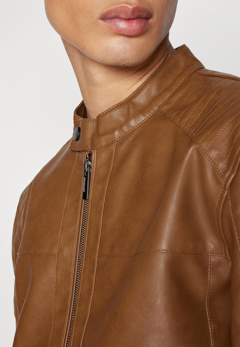 Chaqueta de cuero marrón con cuello alzado, con un cierre frontal y acentos de panel texturizado en los hombros. Acabado suave.