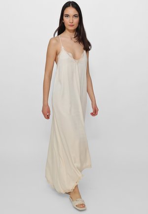 Beige Nachtkleid mit Spitzenbesatz, Spaghettiträgern, fließendem Stoff und V-Ausschnitt, das eine sanfte Drapierung und einen leicht gerafften Saum aufweist.