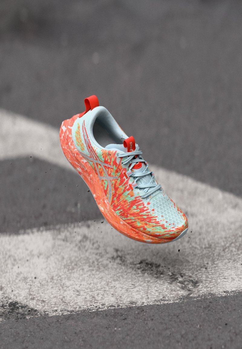 Chaussure de course bleu clair avec des accents orange et verts à motif, tige en mesh, semelle amortie et languette rouge à l'arrière.