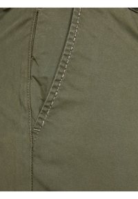 Tissu vert olive avec une texture lisse, présentant des coutures apparentes le long d'une couture latérale et une ouverture de poche en diagonale.