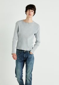 Długo rękawowy, jasnoszary, prążkowany T-shirt z okrągłym dekoltem, w połączeniu z niebieskimi dżinsami o lekkim przetarciu i kontrastowym przeszyciu.