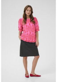 Blusa rosa brillante con motivo testurizzato e maniche a palloncino, abbinata a una gonna di pelle nera e ballerine rosse. Design semplice e moderno.