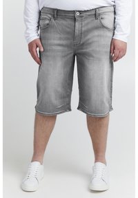 Graue Denim-Shorts mit normalem Schnitt, bis zur Mitte des Oberschenkels, fünf Taschen und einem dezenten, verwaschenen Muster. Kombiniert mit weißen Sneakers.