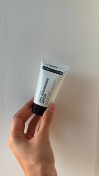 Vit plasttub med svart kork, märkt "20% Niacinamidserum," med minimal text och en snygg design, hålls i en hand.