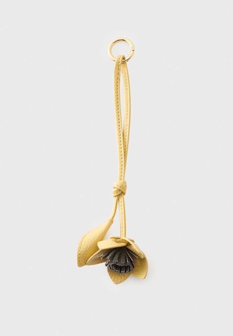 Porte-clés en cuir jaune en forme de fleur avec un anneau doré et une longue lanière en boucle, posé sur un fond clair et uni.