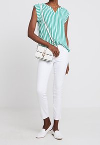 Grøn- og hvidstribet bluse med korte ærmer, parret med hvide slim-fit bukser og hvide slip-on sko. Lille crossbody taske med guld detaljer.