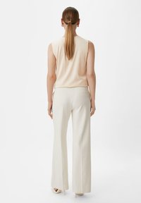 Lichtbeige mouwloze top gecombineerd met crèmekleurige broek met wijde pijpen; zachte textuur, minimalistisch ontwerp en subtiele zijzakdetails.