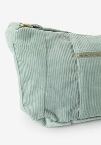 Sac en velours côtelé vert pâle avec une surface texturée, doté d'une fermeture éclair dorée et d'une petite poche externe. Forme rectangulaire avec des bords arrondis.