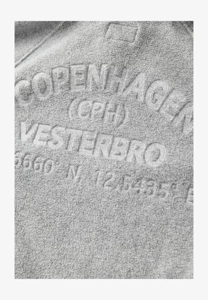 Harmaa fleece-kangas, jossa on koholle painettu teksti: "KOPENHAGEN (CPH) VESTERBRO 5660'N 12.5435'E." Pehmeä tekstuuri ja vaalea väri.