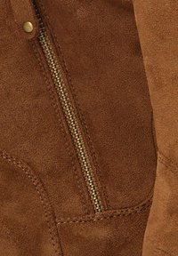 Tela de ante marrón con una cremallera dorada visible y detalles de costura. Presenta una textura suave y bordes redondeados.
