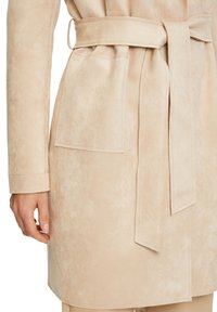 Beige mokkanahkainen takki, jossa on vyötärövyö, sivutaskut ja sileä pinta, keskipitkä leikkaus ja siistit ompelusomisteet.