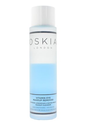 Bouteille cylindrique transparente contenant un liquide bleu, étiquetée "Oskia Démaquillant pour les Yeux à la Vitamine", avec du texte noir et blanc et un capuchon blanc.