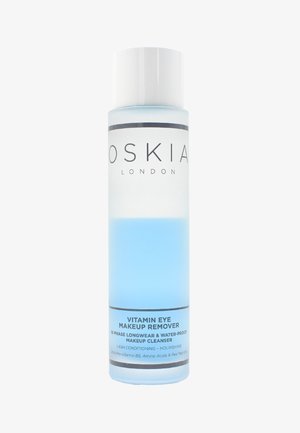 Bouteille cylindrique transparente contenant un liquide bleu, étiquetée "Oskia Démaquillant pour les Yeux à la Vitamine", avec du texte noir et blanc et un capuchon blanc.