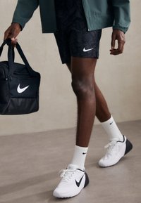 Şorturi Nike negre cu un model subtil, logo-ul Nike alb, adidași albi cu accente negre și o geantă de sport neagră cu un logo alb.