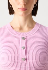 Rosa ribbestrikket topp med rund hals, prydet med tre dekorative hjerteformede knapper med rhinestones på stolpen.