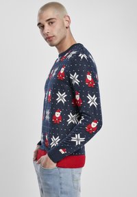 Pull en tricot bleu marine avec motifs rouges de Père Noël et flocons de neige blancs. Poignets et taille rouges côtelés, texture douce, col rond.