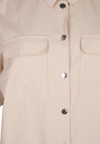 Camisa beige de botones con rayas blancas verticales, cuello, dos bolsillos en el pecho y botones a presión plateados. Textura de tela suave.