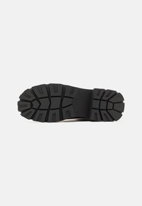 Semelle de chaussure en caoutchouc noir avec des profondes rainures, des motifs hexagonaux et un talon renforcé. Surface lisse avec une texture durable pour l'adhérence.