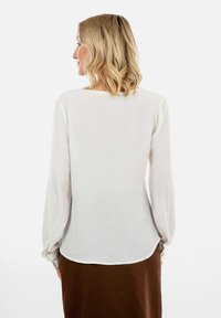 Weiße Bluse mit langen Ärmeln und rundem Ausschnitt, aus leichtem Stoff gefertigt, mit elastischen Bündchen und einer dezenten, fließenden Passform.