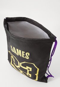Saco de cordão preto com um cordão roxo, apresentando uma grande impressão amarela com "JAMES" e o número "23" na frente. Material texturizado.