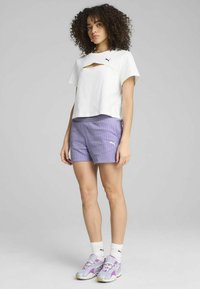 White cropped shirt with a cutout detail, paired with light purple pinstriped shorts. Footwear features purple accents. White socks.