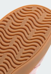Rubber sneaker sole in orange with a textured wavy pattern, featuring hexagonal details and solid pink upper section.
