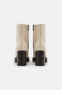 Stivaletti alla caviglia in pelle verniciata beige con punta quadrata e tacco a blocco in legno scuro, dotati di chiusura con zip sul retro. Texture liscia e lucida.