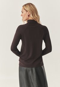 Donkerbruin sweatshirt met een geribbeld kraag, aansluitend ontwerp, lange mouwen en een zachte textuur; gedragen met een zwarte leren rok, wat een ontspannen silhouet laat zien.
