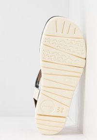 Semelle blanche en caoutchouc avec motif texturé, dessus en daim marron et sangles noires. Taille indiquée comme 38. Semelle conçue pour l'adhérence et la stabilité.