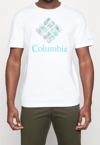 Vit bomullströja med en turkos och flerfärgad Columbia-logotypgrafik på framsidan. Kortsleeves och rundad halsdesign.