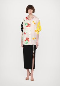 Lillelise mustriga blouse, millel on kollased ja mustad varrukad, koos musta seelikuga, millel on külgmine tõmblukk. Sile kangas, kuni põlve ulatuv disain.