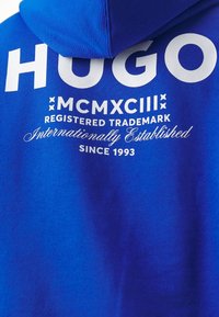 Felpa blu con ampio testo bianco "HUGO", con ulteriori marchiatura in scrittura bianca e numeri romani, realizzata in tessuto leggero e testurizzato.