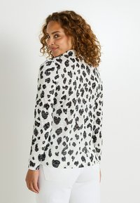 Haut à manches longues en imprimé léopard noir et blanc avec un tissu texturé. Encolure ronde, coupe ajustée et détails de couture discrets à l'ourlet.