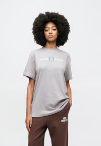 Sivá tričko Nike Shox s krátkymi rukávmi a okrúhlym výstrihom, s výrazným bielym logom na hrudi.